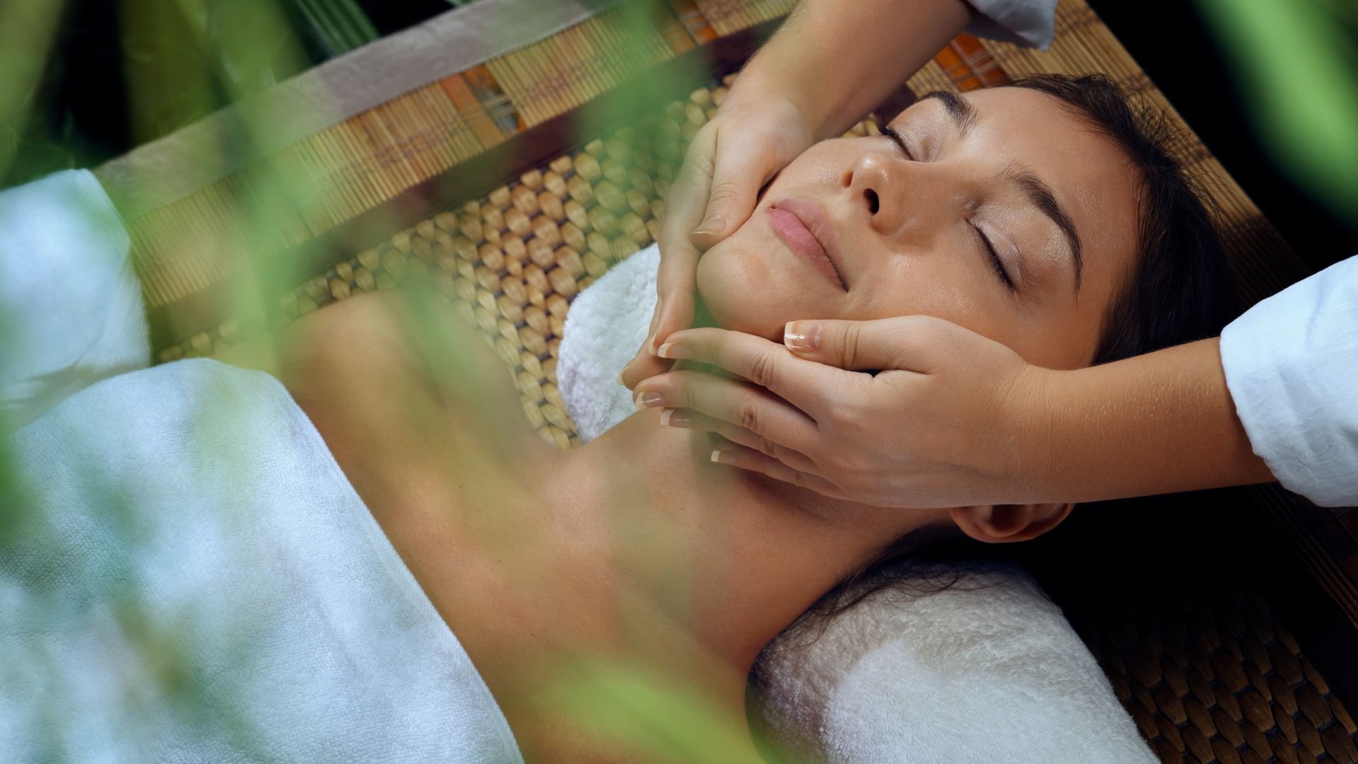 Relaxed person receiving facial massage at spa with soft green background