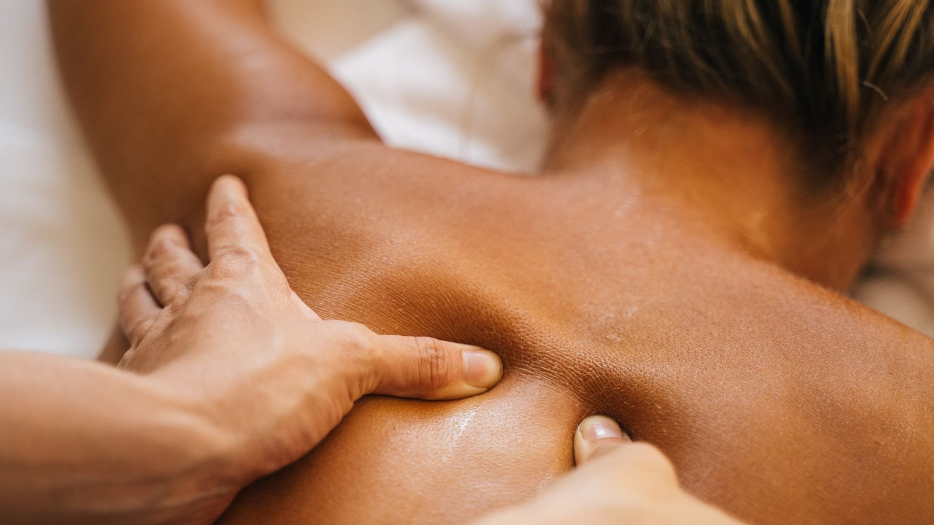 Hands performing deep tissue massage on person's back and shoulder