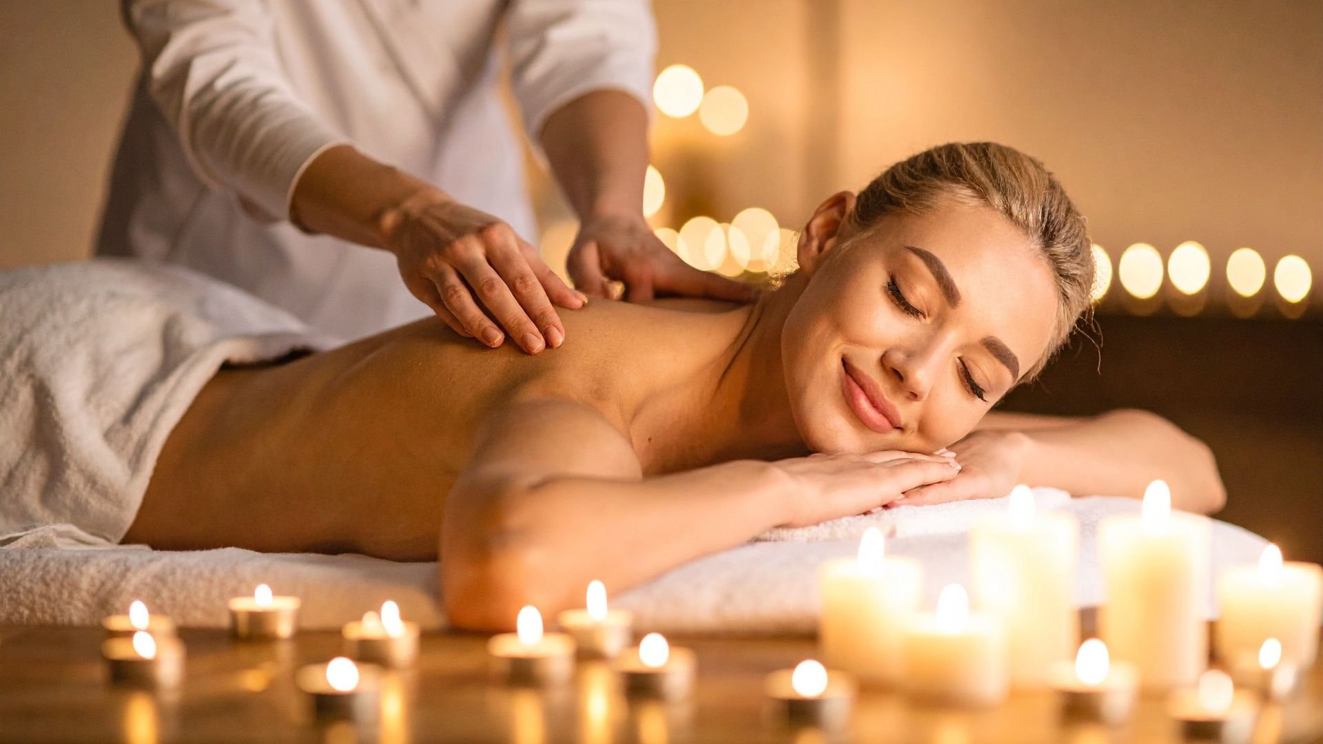 Relaxed person receiving massage surrounded by candlelight in spa setting