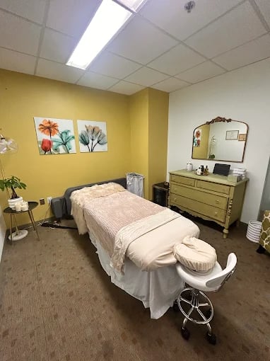 Massage therapy room with white bed, yellow walls, and floral artwork